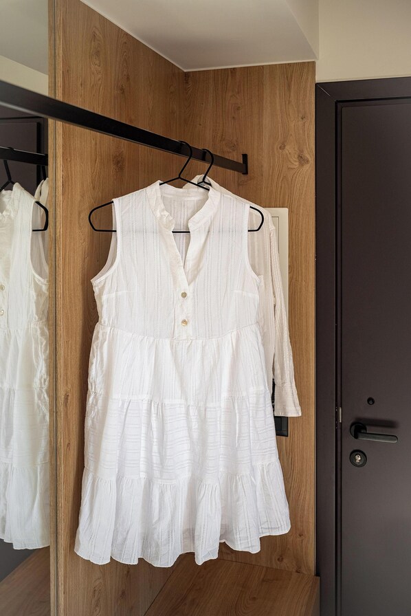 A white dress hanging on a wooden hanger in a closet.