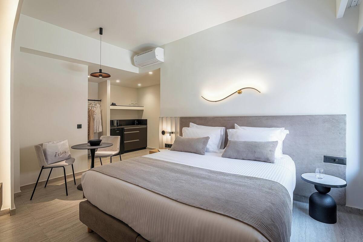 A modern hotel room with a large bed, a small round table, a chair, and a separate dining area.