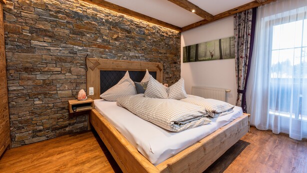 Un dormitorio con pared de piedra, estructura de cama de madera y mesita de noche con una lámpara de sal.