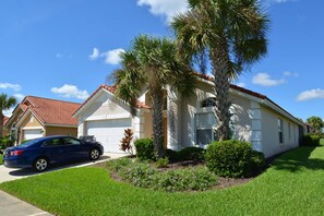 A two-story house with a red-tiled roof, a garage, and a driveway with a parked car. - The Beauty of Solana Near Disney and Universal (Davenport)