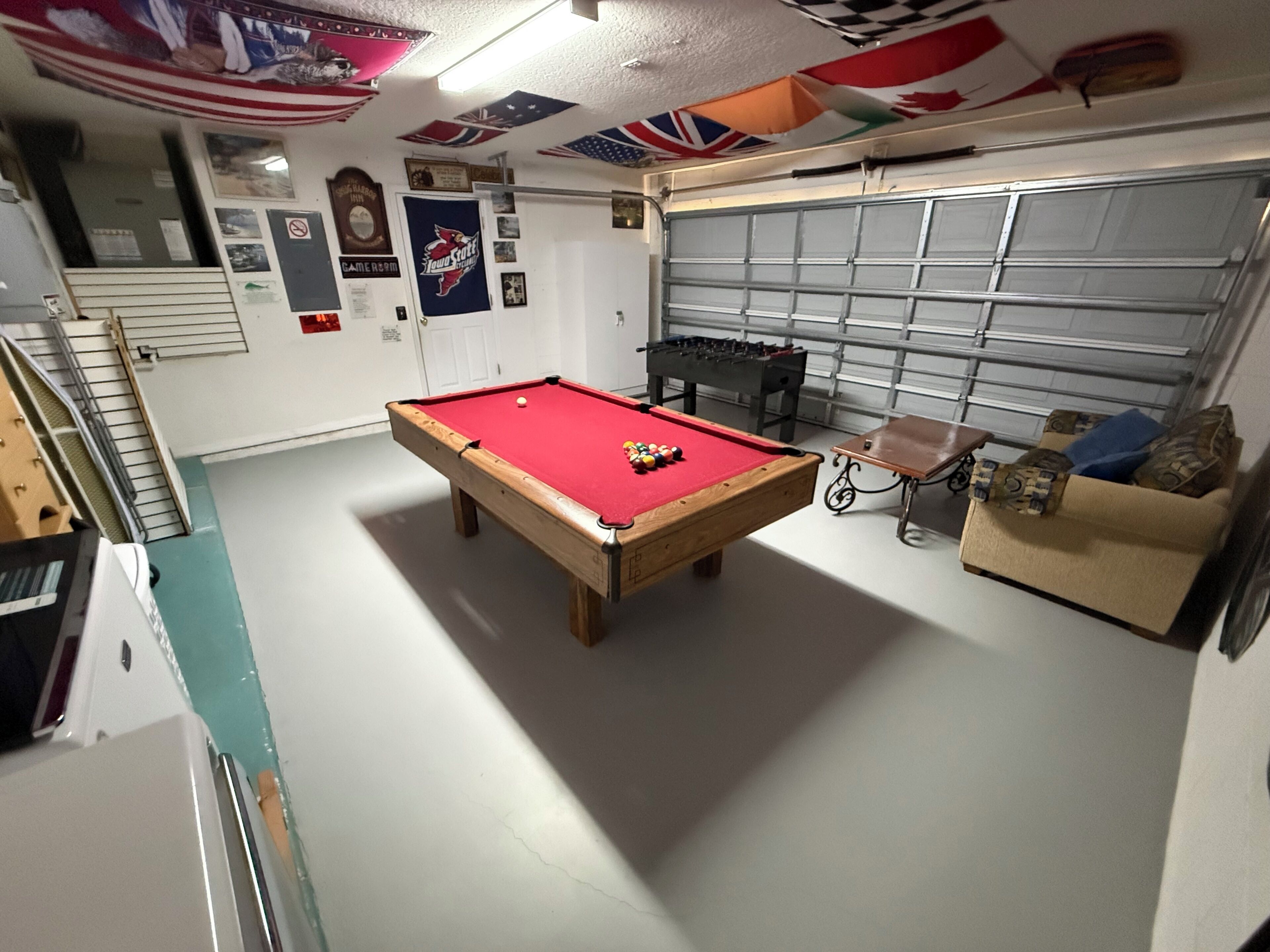 A pool table in a room with a garage door, a sofa, and various wall decorations.