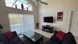A living room with a ceiling fan, a flat-screen TV on a black stand, a glass coffee table, and dark sofas with red cushions. - The Beauty of Solana Near Disney and Universal (Davenport)