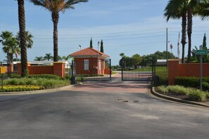 A gated entrance with a small red kiosk, palm trees, and a clear sky. - The Beauty of Solana Near Disney and Universal (Davenport)
