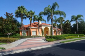 Edificio de dos pisos con tejido rojo y puertas arqueadas, rodeado de palmeras y un jardín cuidado.