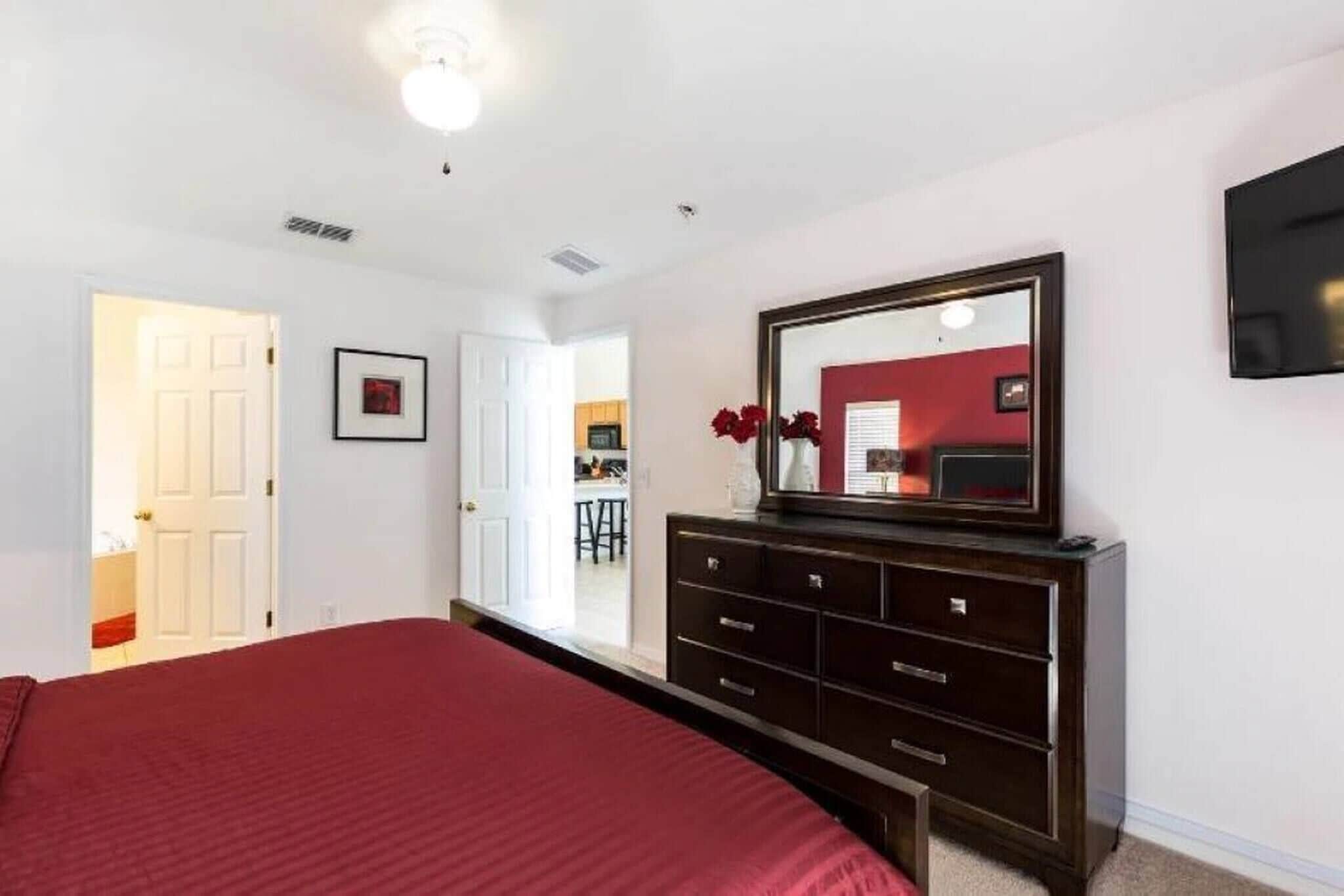 A bedroom with a large bed, a dresser, a mirror, and a TV on the wall.