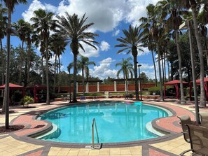 A swimming pool surrounded by palm trees and red canopies, with a clear blue sky above. - The Beauty of Solana Near Disney and Universal (Davenport)