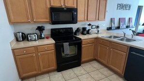 A compact kitchen with wooden cabinets, a black stove, a microwave, a sink, and a trash bin. - The Beauty of Solana Near Disney and Universal (Davenport)