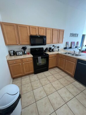A compact kitchen with wooden cabinets, a black stove, a microwave, a sink, and a trash bin. - The Beauty of Solana Near Disney and Universal (Davenport)
