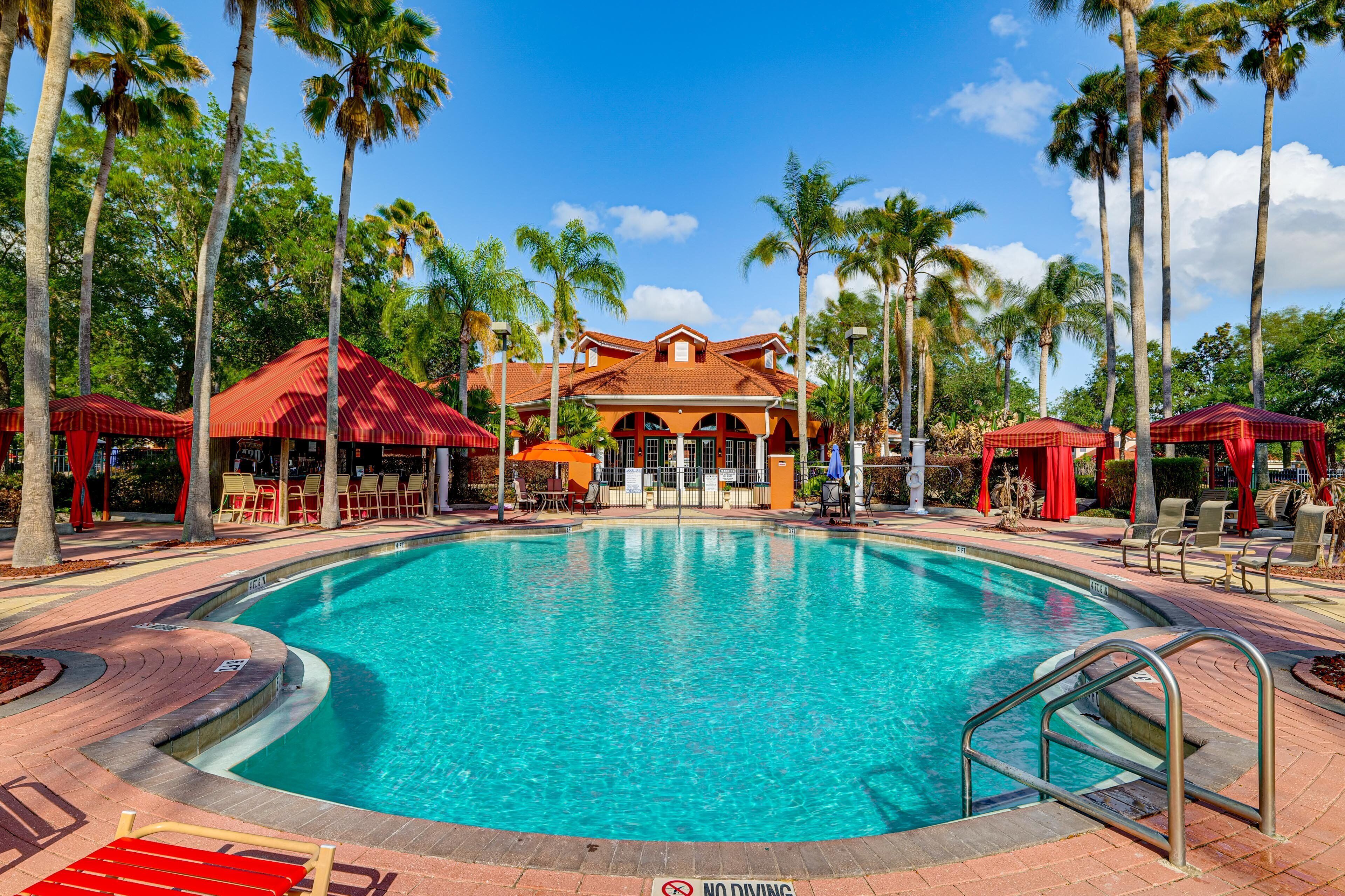A swimming pool with a no diving sign, surrounded by palm trees and a building with a red roof.