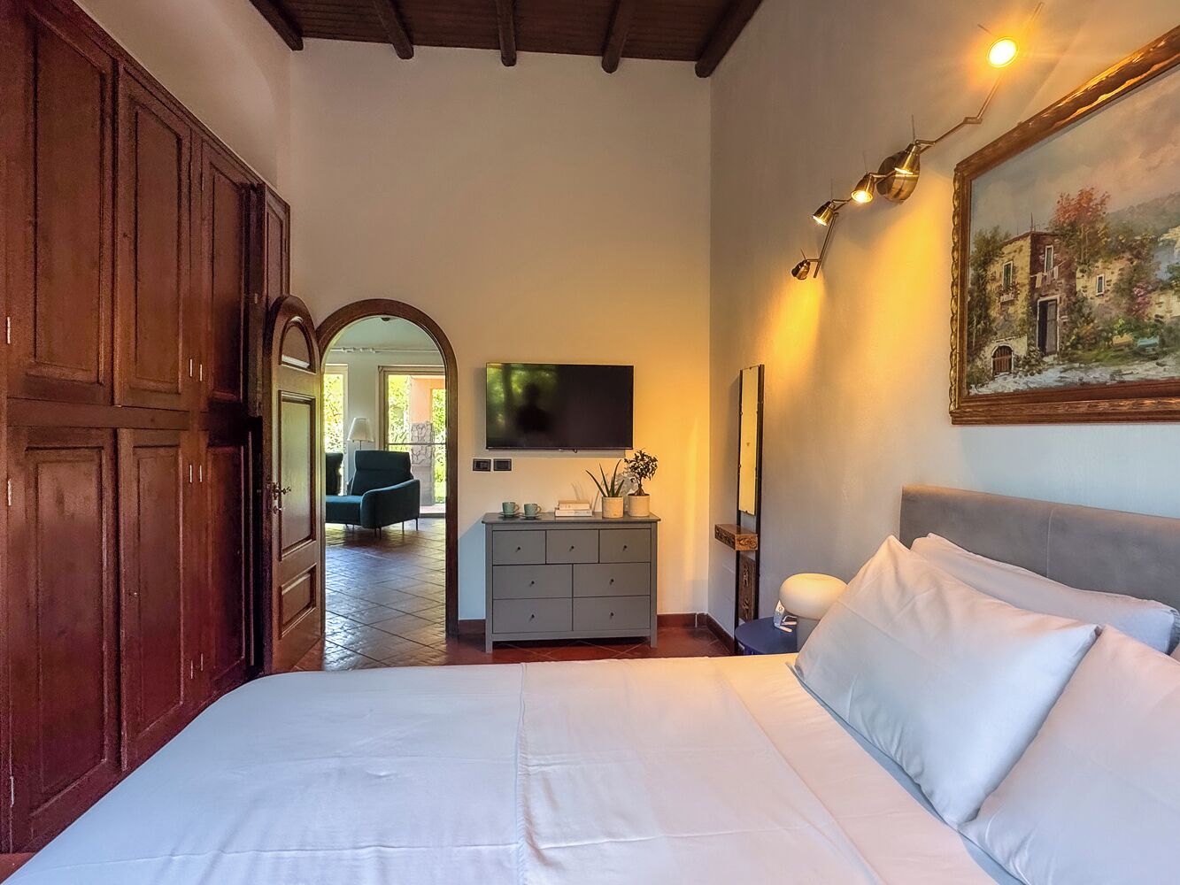 A bedroom with a large bed, a dresser, a TV, and a painting on the wall.