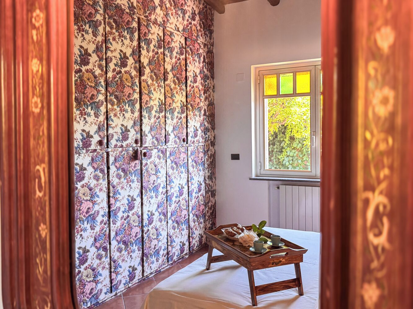 A room with a floral-patterned sliding door, a wooden table with a tray of items, and a window with a view of greenery.