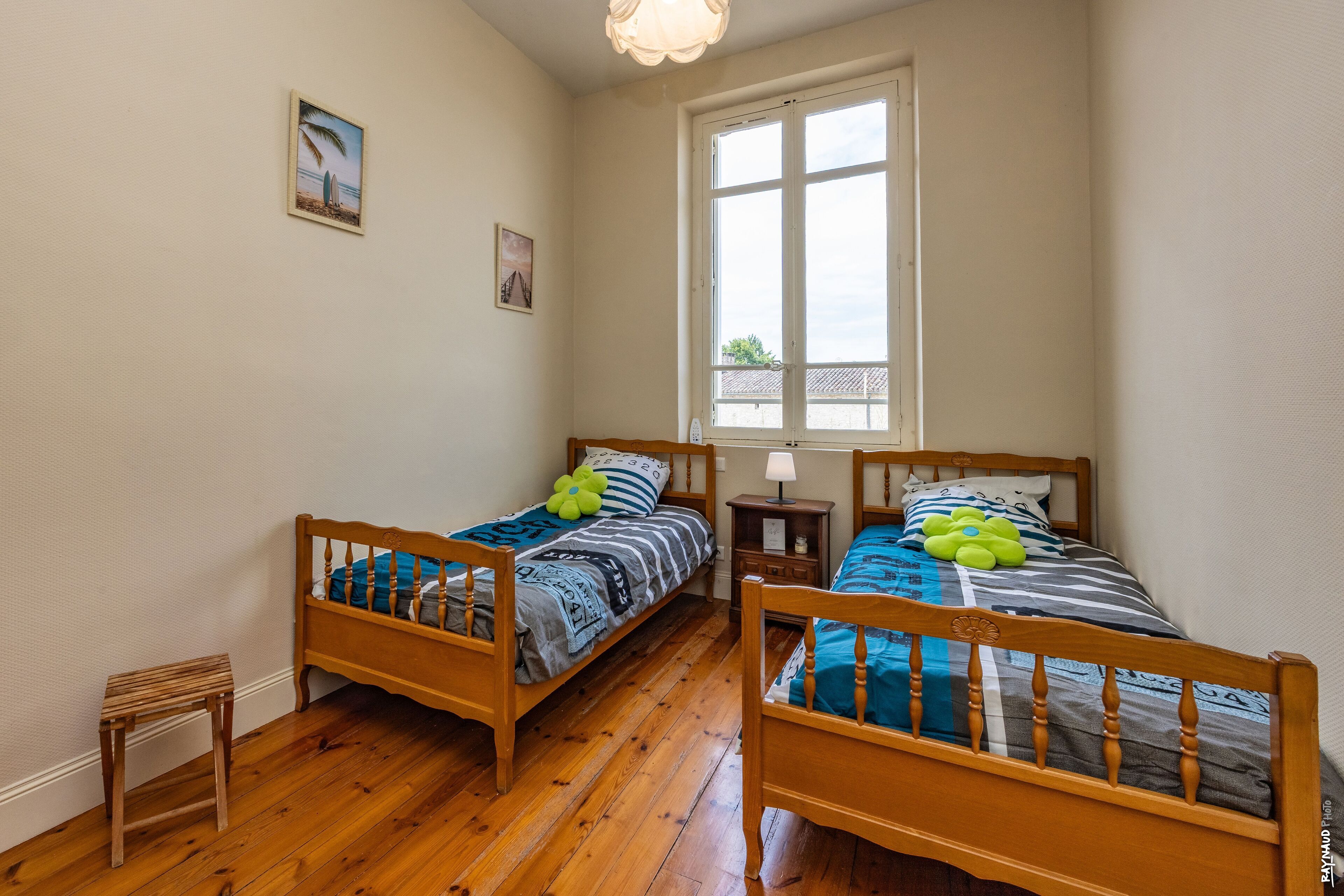 A room with two wooden beds, a small table, a nightstand, and a window with a view of buildings outside.