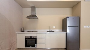 A compact kitchen with a built-in oven, a stainless steel refrigerator, and a modern range hood. - Kennah Studio | Villette Sodic, New Cairo (New Cairo)