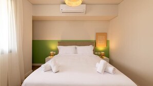 A hotel room with a large bed, white bedding, a green accent wall, two bedside tables with lamps, and an air conditioning unit on the wall. - Kennah Studio | Villette Sodic, New Cairo (New Cairo)
