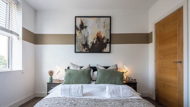 Un dormitorio ordenado con una cama grande, una mesita de noche con lámpara y una puerta de madera.