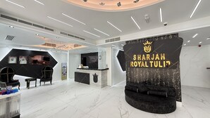 A modern hotel lobby with a reception desk, seating area, and a large wall with the hotel's name. - Royal Tulip Dancenter Suites Sharjah (Sharjah)
