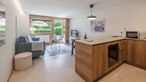 A modern kitchen with a wooden island, a dining area with a grey sofa, and a large window overlooking a garden.