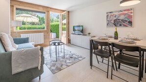 A modern living room with a sofa, a dining table with chairs, a TV, and a painting on the wall.