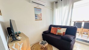 A living room with a dark-colored sofa, a wooden side table with a decorative item, a woven rug, and a poster on the wall.