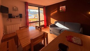 Una habitación acogedora con una mesa de comedor de madera, un sofá gris, una cortina roja y vistas a un paisaje nevado por la ventana.