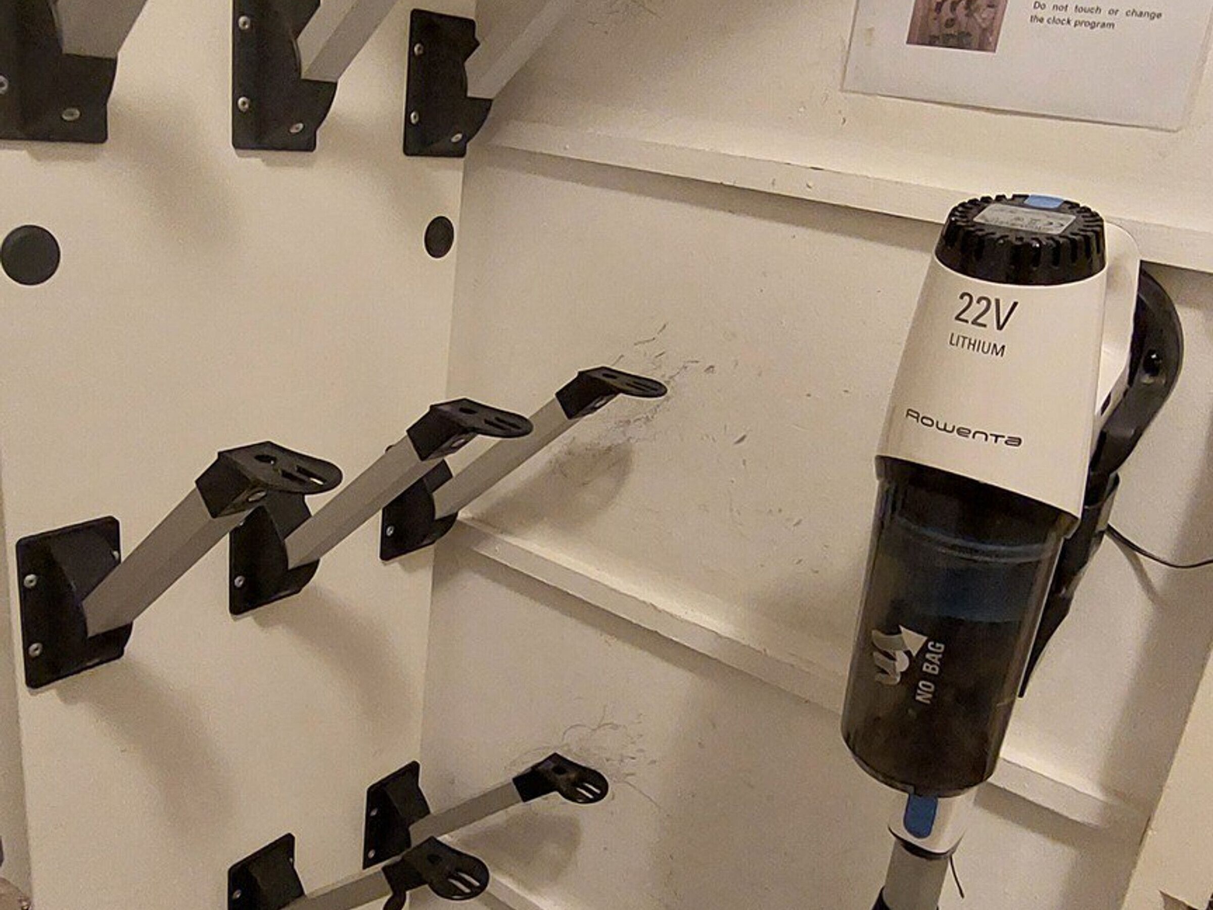 Een muur met een bevestigde fietsendrager en een fles met de tekst '22V LITHIUM' en een bordje 'GEEN TASSEN'.