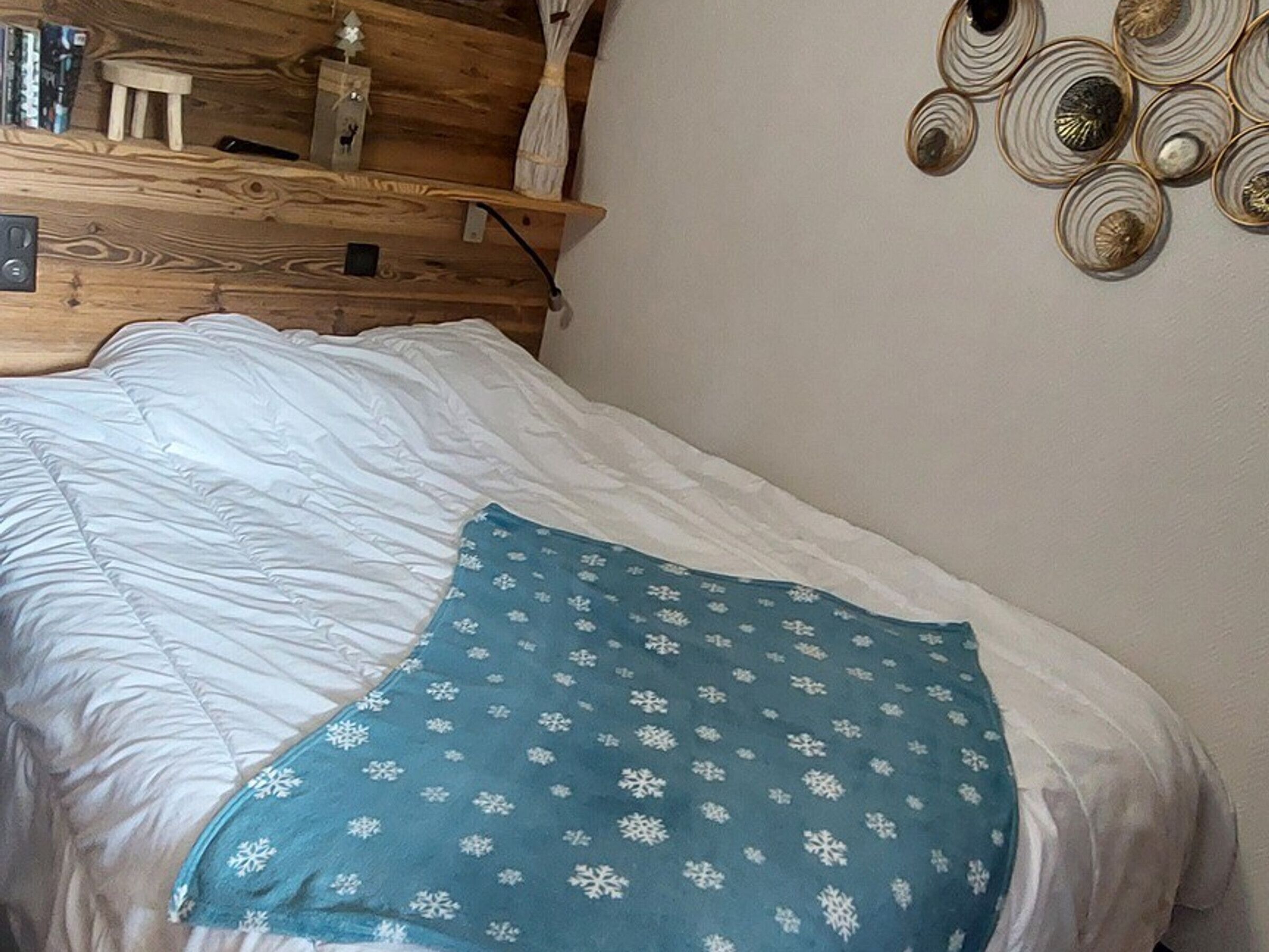 A bed with white bedding and a blue pillow with snowflake patterns.