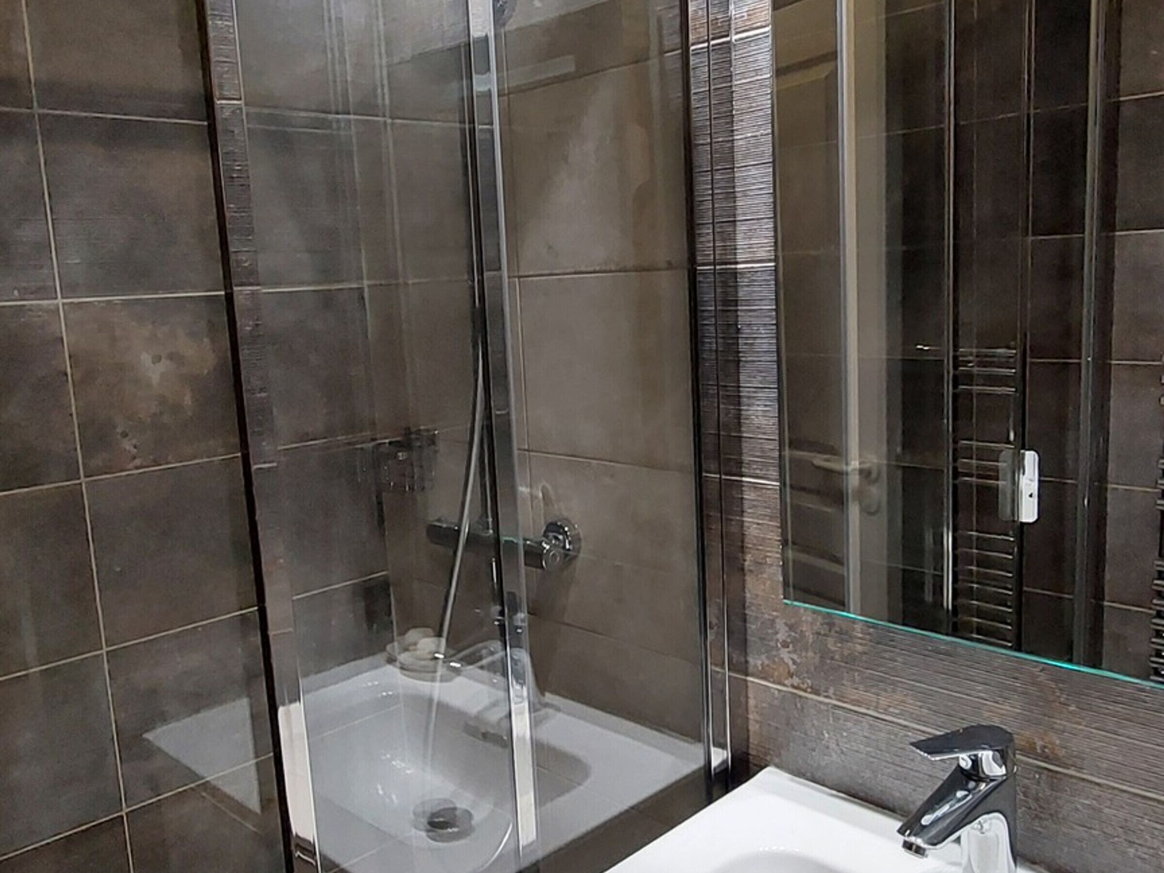 Un baño moderno con ducha envuelta en vidrio, un lavabo blanco y un espejo con marco de cristal.