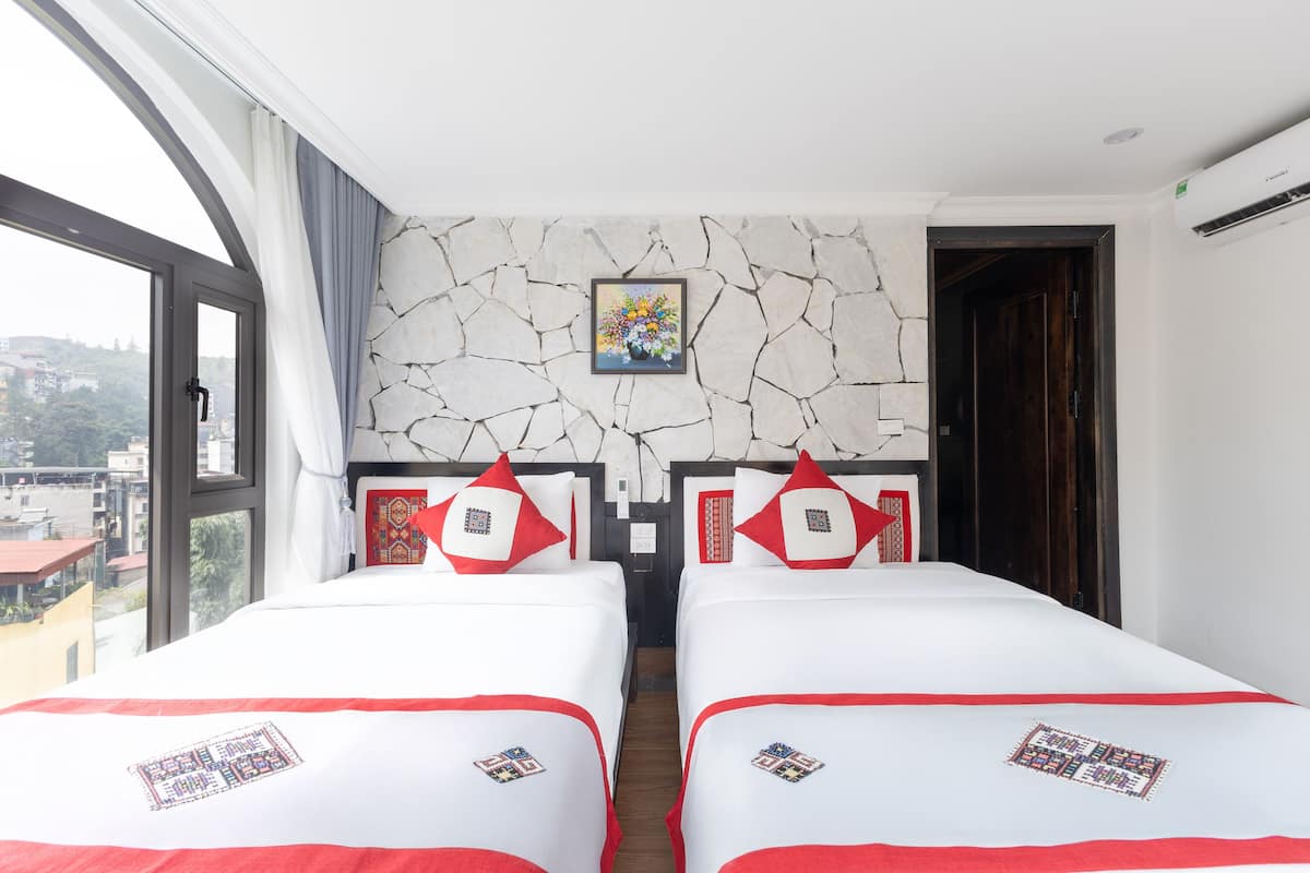 A hotel room with two beds, a large window, a stone wall, and a painting.