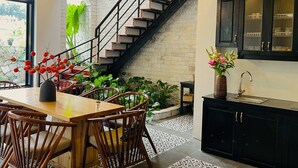 Une cuisine moderne avec des meubles de couleur sombre, une table à manger en bois avec des chaises, un escalier avec des marches rouges et une vue sur la verdure à l’extérieur.