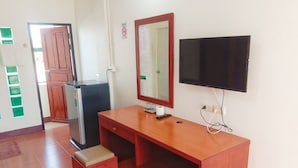 Una habitación con un escritorio de madera, un televisor negro, un espejo, un refrigerador y un taburete pequeño.