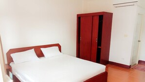 Un dormitorio con cama de madera, ropa de cama blanca, un armario y suelo de baldosas.