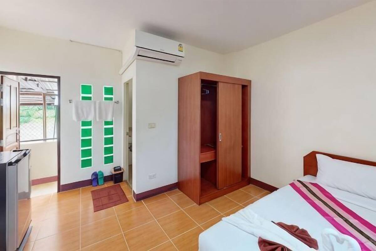 A bedroom with a bed, a wardrobe, a desk, and an air conditioning unit.