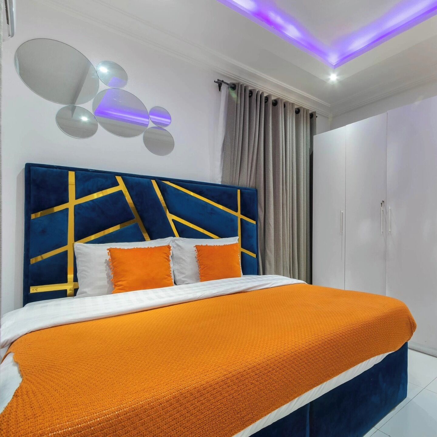 A modern bedroom with a blue and gold headboard, an orange bedspread, and a ceiling light fixture.