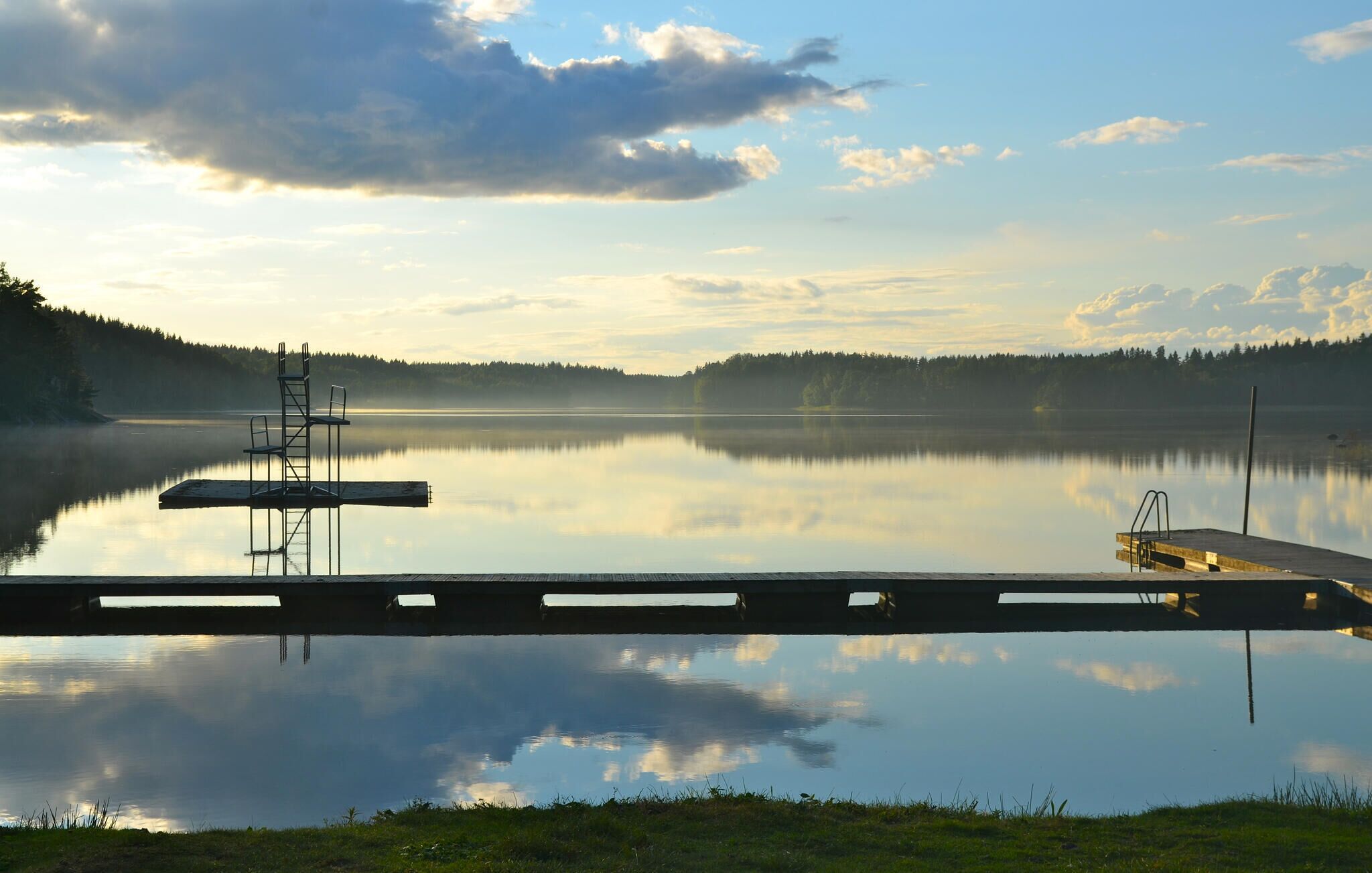 Un lac paisible, avec un quai et une chaise, entouré d’arbres.