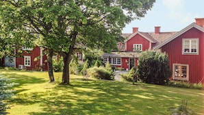 A red wooden house with a well-maintained lawn and a tree in the foreground.
