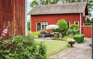 Una casa in legno rossa con tetto a tegole, un giardino con diverse piante e fiori, mobili da esterno e un vialetto che conduce alla casa.