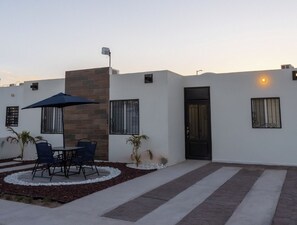 A modern building with a patio area featuring a table and chairs, a small garden, and a black door.
