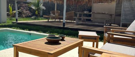 A wooden outdoor seating area with a pool and a thatched roof structure.