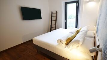 Une chambre à coucher avec un lit, un téléviseur fixé au mur, une fenêtre donnant sur un beau paysage et un plancher en bois.