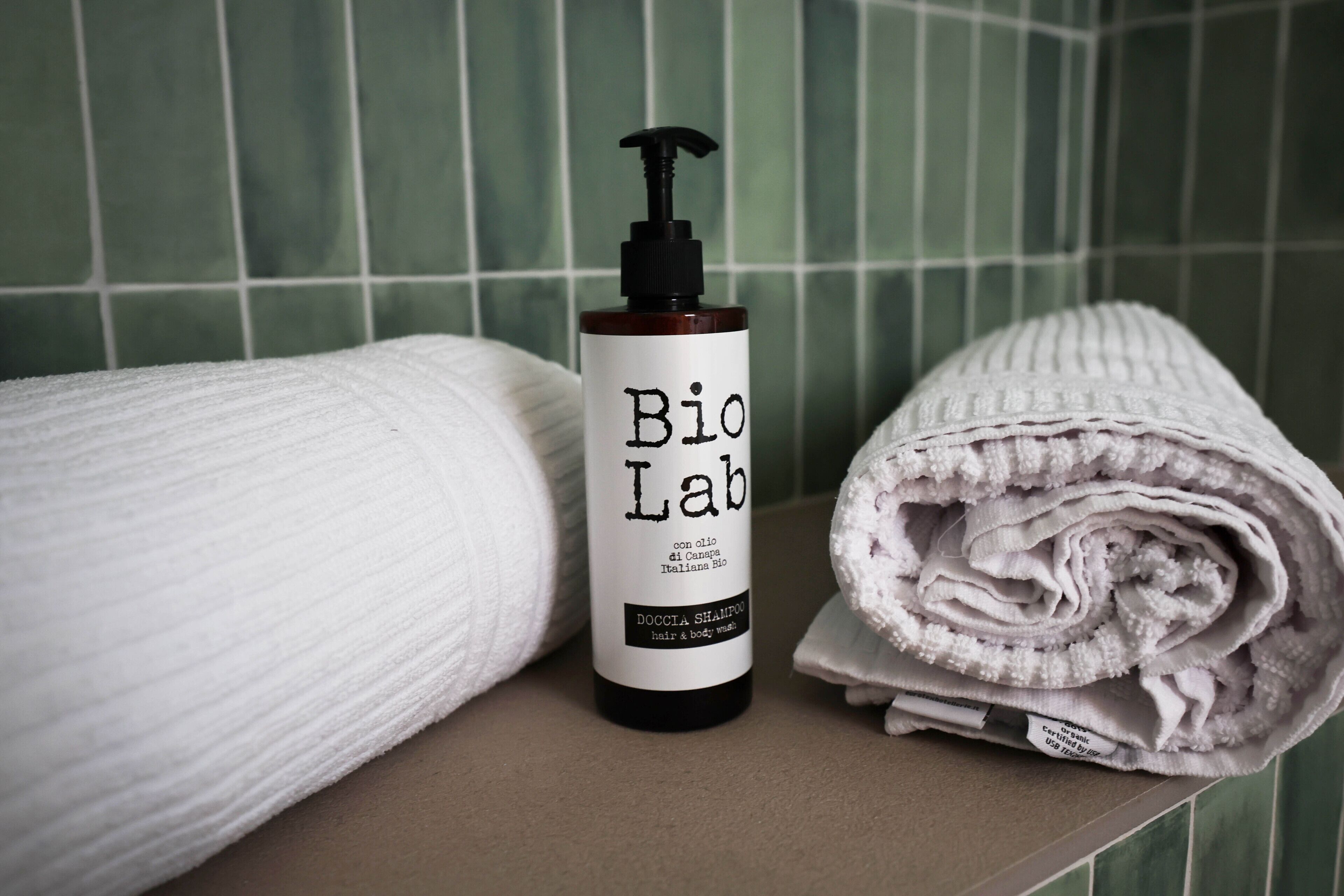 Ein Badezimmer mit grünen Fliesen, einem weißen Handtuch und einer Flasche Bio Lab Ha- und Körperwäsche.