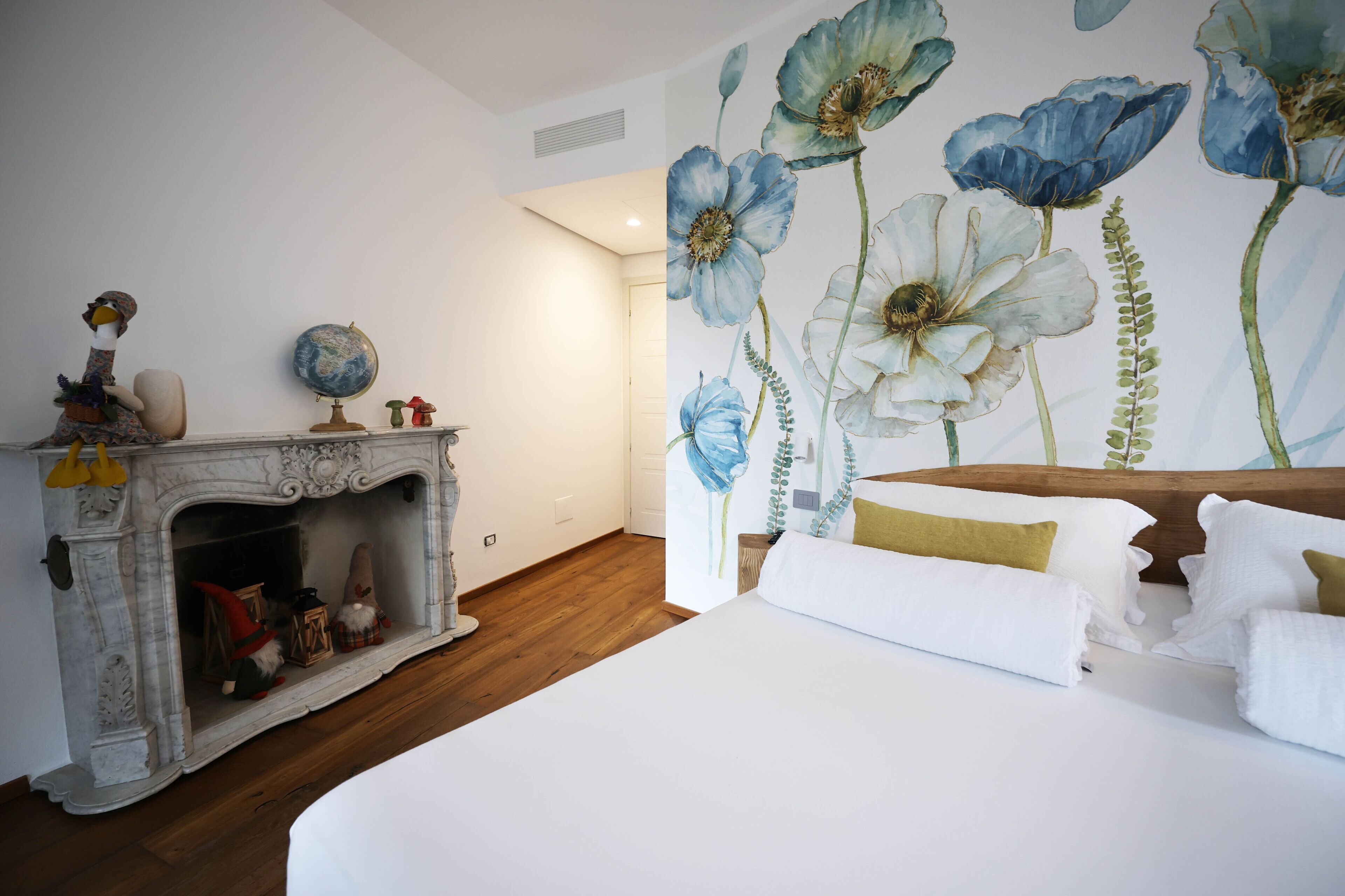 A bedroom with a large bed, a fireplace with gnome decorations, and a floral mural on the wall.