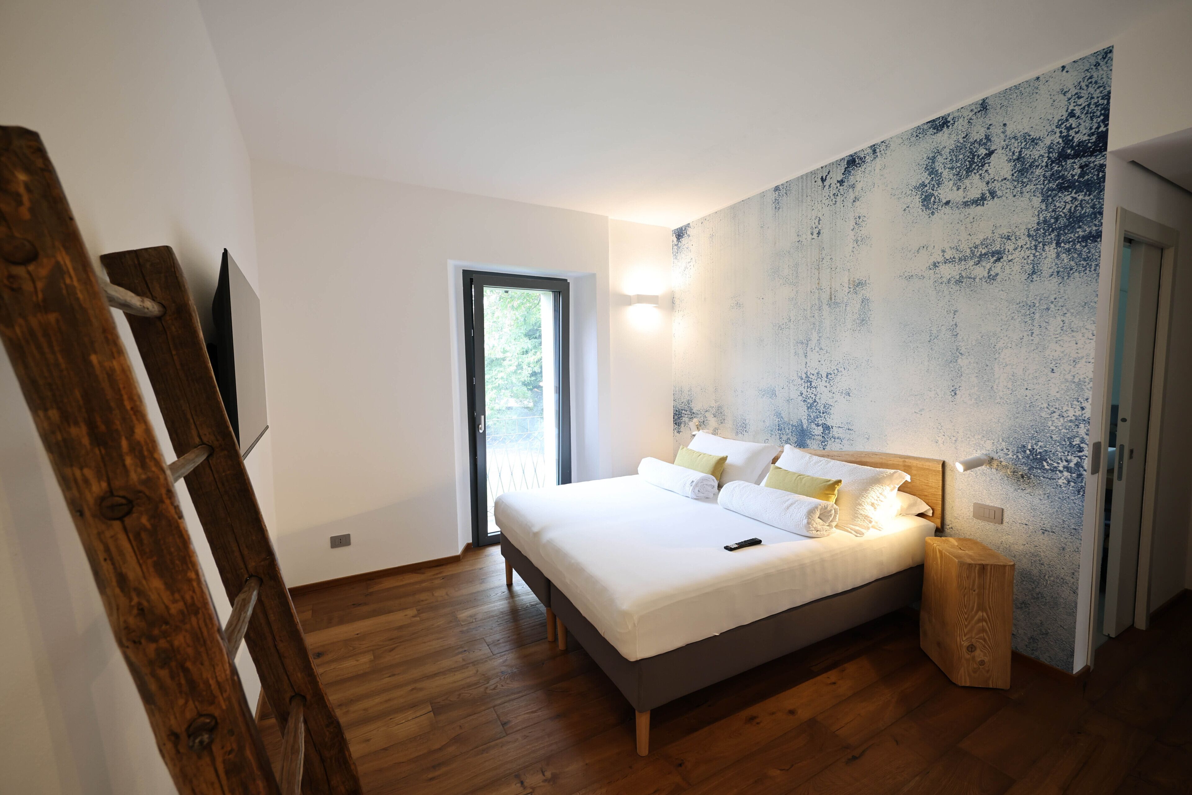 A bedroom with a bed, wooden floor, a window, and a wall with a textured design.
