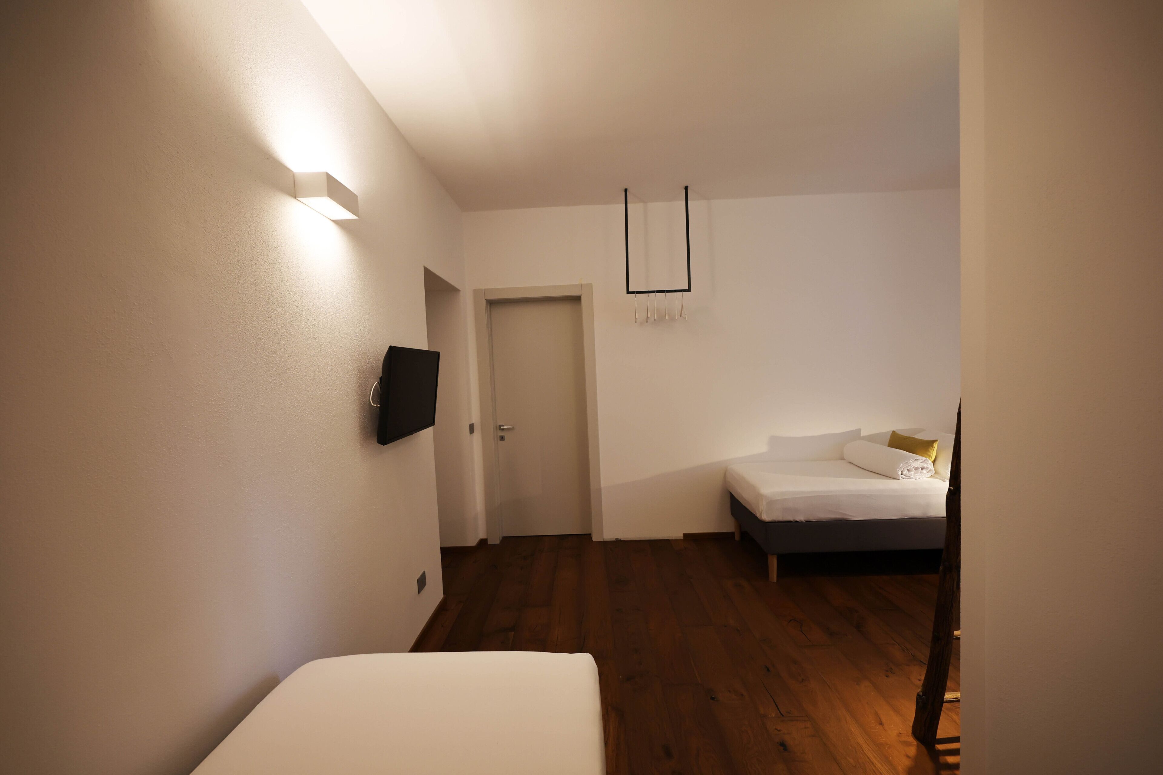 A bedroom with a bed, a door, and a wall-mounted TV.