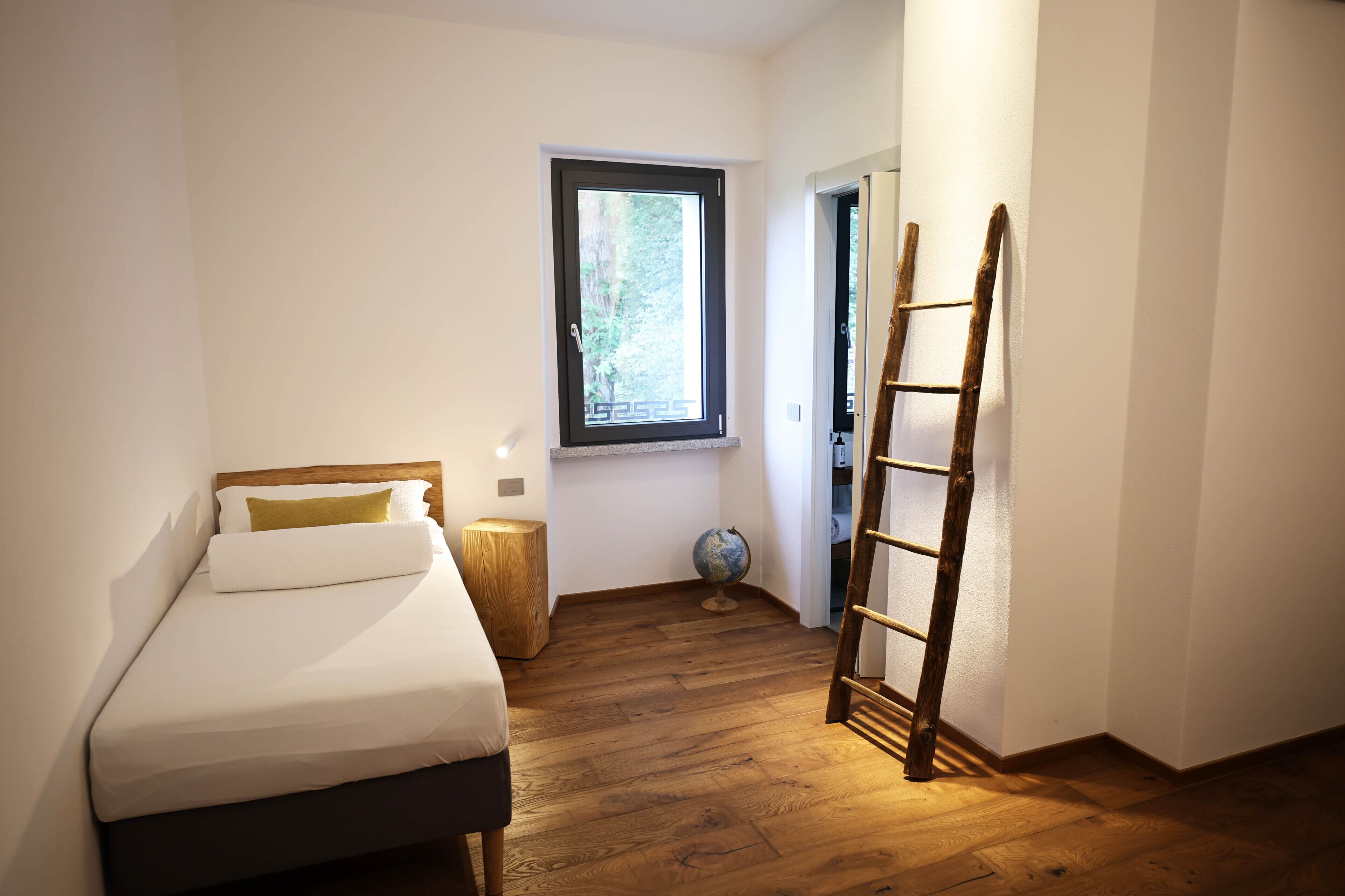 A bedroom with a bed, a window, a globe, and a wooden ladder.