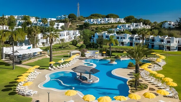 A resort with a large pool, sun loungers, and a view of the sea.