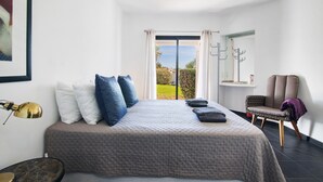 A bedroom with a bed, a chair, a lamp, and a view of the outdoors.