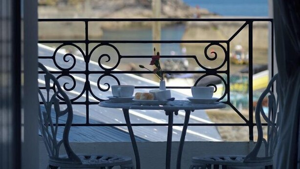 Ein Balkon mit Tisch und Stühlen, der auf eine Küstenlandschaft mit felsigem Gelände und dem Meer blickt.