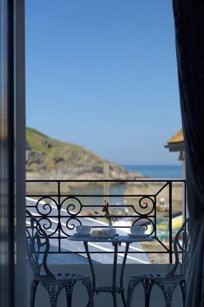 A balcony with a table and chairs, overlooking a coastal area with a rocky landscape and the sea. - The Slipway  (Port Isaac)