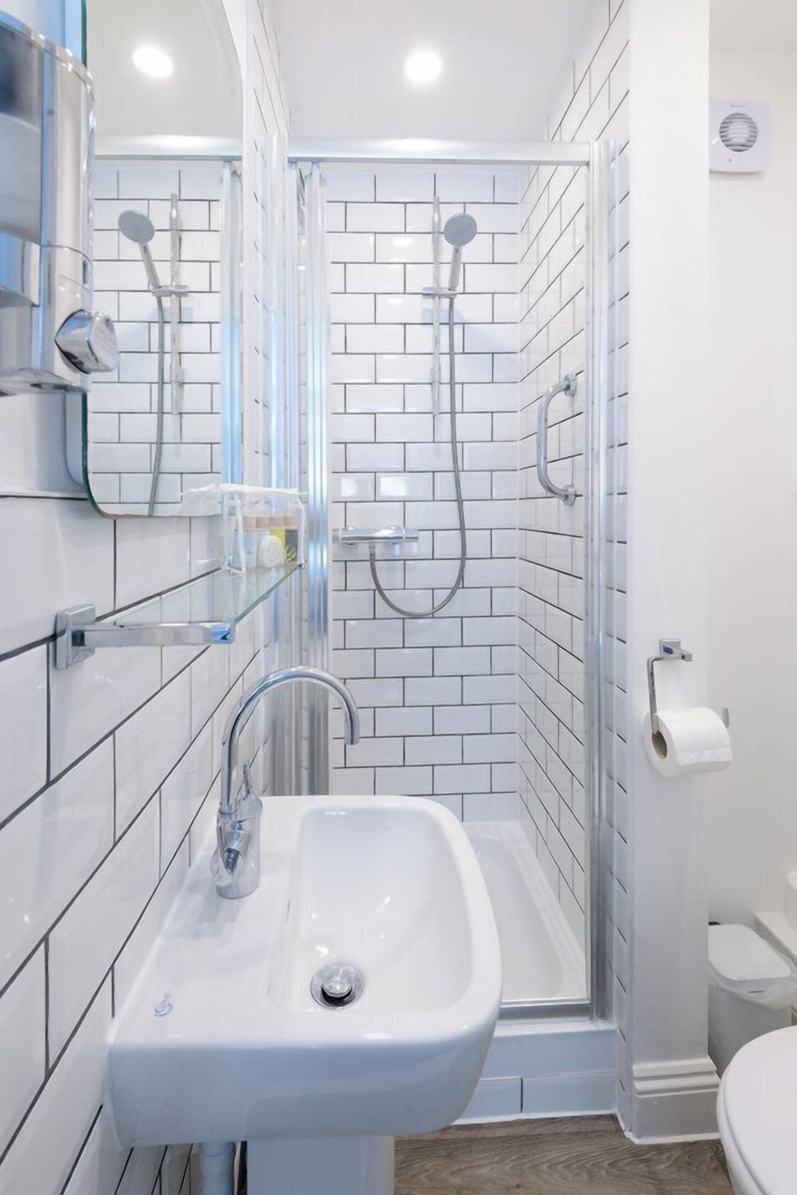 Ein modernes Badezimmer mit Duschkabine in weißen Fliesen, Waschbecken mit Spiegel und Toilette.