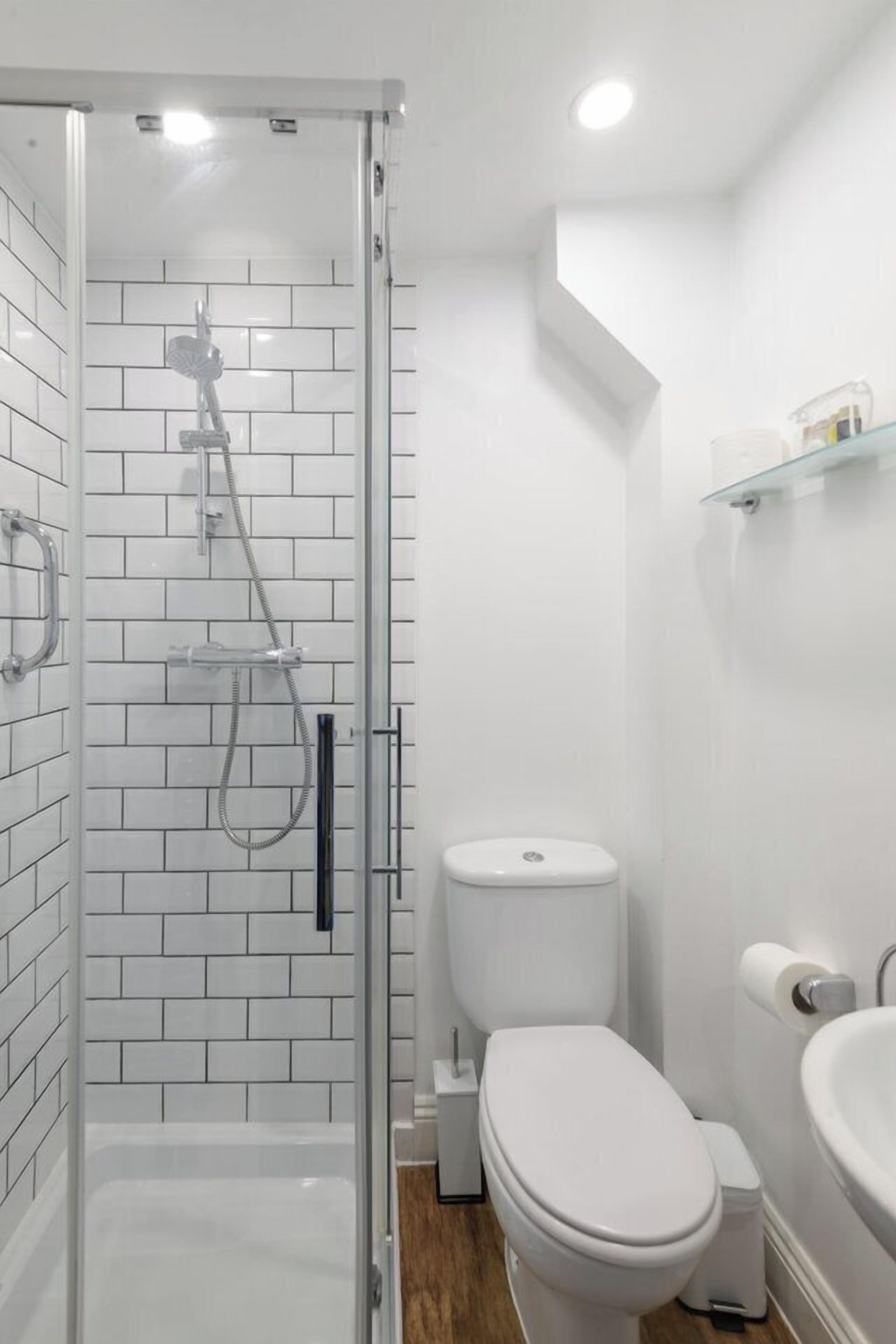 Un baño moderno con ducha envuelta en vidrio, inodoro blanco y lavamanos.